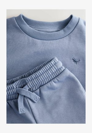 Sweatshirt bleu clair avec un col côtelé et un petit logo de dinosaure. Le pantalon de jogging assorti possède une taille élastique et un cordon de serrage.