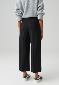 Zwarte wijde broek met een zachte textuur, hoge taille en een enkele achterzak. Gecombineerd met witte sneakers met zwarte accenten.