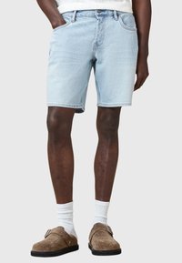 Shorts di denim blu chiaro con taglio diritto, cinque tasche e cuciture semplici. Indossati con calzini bianchi e scarpe slip-on in camoscio marrone.