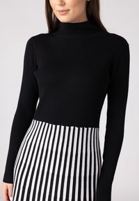 Haut noir en maille côtelée avec un col montant, se transformant en une jupe rayée blanche et noire. Doté de manches longues et d'une silhouette ajustée.