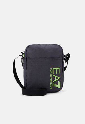 Sac à bandoulière en tissu gris foncé avec fermeture zippée, ornée d'un logo vert néon et d'une sangle ajustable. Design compact et rectangulaire.