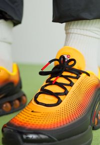 Nike sneakers featuring a gradient design from yellow to orange, mesh material, black laces with red accents, and visible cushioning pods.