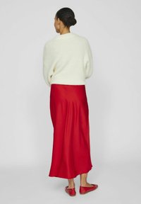 Pull blanc, jupe en satin rouge et ballerines rouges. Le pull a une coupe ample, la jupe est longue et fluide. La texture est douce et lisse.