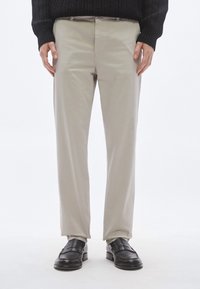 Lys beige bukser med en glat tekstur, lige snit og lynlåslukning; kombineret med sorte læderloafers.