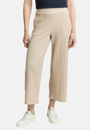 Pantalons larges beiges, coupés, en tissutexturé avec un motif en relief, associés à des baskets blanches. Ceinture élastique pour le confort.