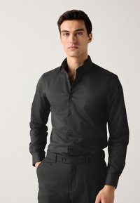 Camicia nera a maniche lunghe in tessuto liscio, con colletto classico, chiusura con bottoni sul davanti e pantaloni neri abbinati.