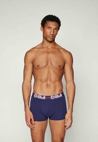 Marineblå boxershorts med en kontrasterende linning som har en rød og hvit logo, laget av strekkbart stoff, tettsittende design.