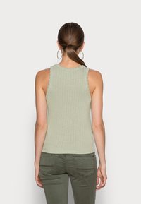 Jasnozielony, prążkowany top na ramiączkach z okrągłym dekoltem i bez rękawów, zestawiony z oliwkowozielonymi dopasowanymi spodniami. Prosty i dopasowany.