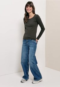 Haut à manches longues vert foncé associé à un jean bleu ample et des baskets argentées, avec un col rond et des détails minimalistes.