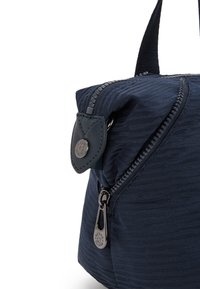 Marinblå tygväska med en texturerad design, framträdande dragkedjestängning och en läderdetalj med en silverfärgad knapp.