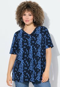 Námořnická modrá halenka s krátkými rukávy a výstřihem do V obsahující opakující se vzor světle modrého textu. Volný střih s mírným skladem podél výstřihu.
