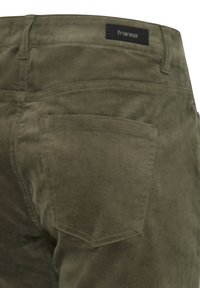 Vue arrière d'un pantalon en velours côtelé vert olive avec une seule poche arrière visible et une étiquette de marque noire "fransa" au-dessus de la poche.