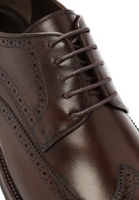 Chaussure habillée en cuir marron foncé avec des perforations de type brogue et un laçage fermé sur un empeigne lisse et poli.