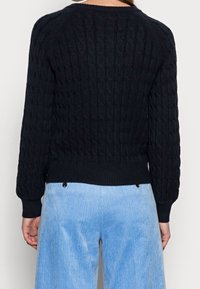 Maglione nero a coste con polsini e orlo a coste, caratterizzato da un motivo a rilievo. Abbinato a pantaloni di velluto a coste azzurri.