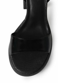 Sandale noire avec une bande supérieure en cuir brillant, une semelle extérieure texturée et un coussin de pied lisse. Design simple avec un bout arrondi.