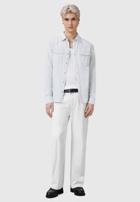 Chemise bleu clair boutonnée portée sur un débardeur blanc côtelé, associée à un pantalon blanc et des chaussures noires. Comprend deux poches poitrine et une coupe ajustée.