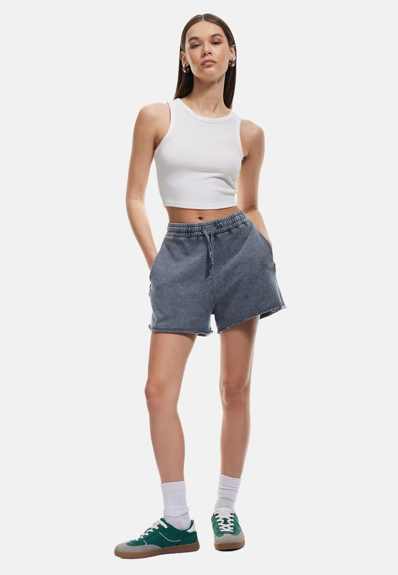 Denimshorts i mørkegrå med elastisk talje og snøre. Parret med en hvid cropped tanktop og grønne sneakers.