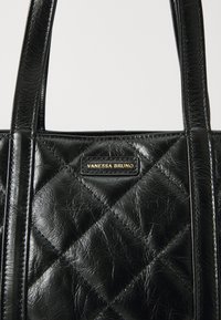 Geantă tote din piele quilted neagră, cu două mânere pentru umăr și o placă cu logo aurie. Textura este lucioasă, cu un finisaj creponat.
