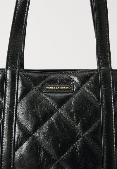 Sac cabas en cuir matelassé noir avec deux poignées et une plaque logo dorée. La texture est brillante avec une finition froissée.
