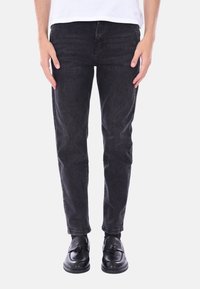 Jeans di denim neri con una vestibilità slim, caratterizzati da una leggera sbiaditura e un classico design a cinque tasche, abbinati a scarpe nere.