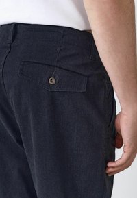 Navy blue pants with a textured fabric, featuring a back pocket with a button closure and a standard waistband.