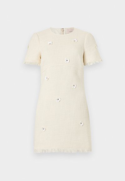 Φόρεμα με κρεμ υφή, κοντά μανίκια, τελειώματα με φουντάκια και μικρές λευκές εφαρμογές ανθών διακοσμημένες με χάντρες.