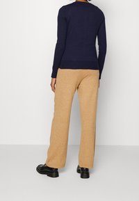 Marinblå tröja med långa ärmar, ribbade muddar och nederkant, kombinerad med löst sittande beige byxor. Bärs med svarta, glansiga skor.