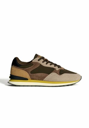 Braune und beige Wildledersneaker mit schwarzen Akzenten, gelber Mittelsohlenstreifen, Schnürverschluss und weißer sowie schwarzer Gummisohle.