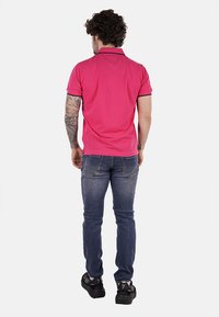 Polo shirt rosa con colletto, maniche corte e bordi scuri. Indossato con jeans blu e sneakers nere, presenta un design aderente.