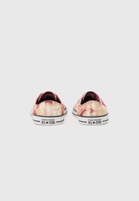 Tenisky Converse All Star s ružovo-krémovým tie-dye vzorom, bielymi šnúrkami a čierno pruhovanými podrážkami; zadný pohľad zobrazuje branding a detaily šitia.