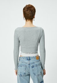 Maglietta grigia a maniche lunghe a coste con design cropped. Caratterizzata da un collo arrotondato e orlo ondulato, abbinata a jeans azzurri a vita alta.