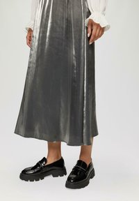 Zwarte lakkloffen met een chunky zool, gecombineerd met een glanzende grijze midi-rok, met een gladde textuur en een uitlopende zoom.