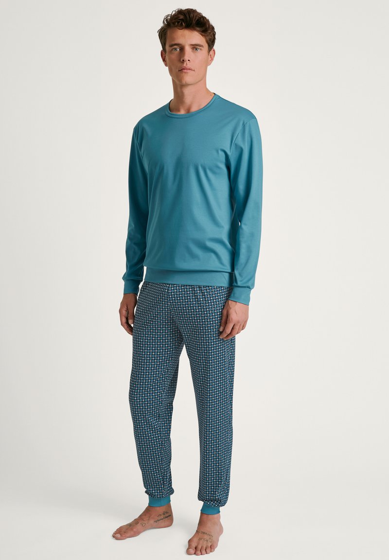 Langarmige blauwe top in combinatie met patroonblauwe pyjamabroeken. De top heeft een ronde halslijn; de broeken hebben elastische boorden en een geometrisch ontwerp.