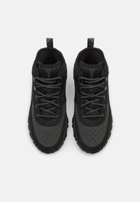Scarpe da atletica nere con tomaia in mesh e suede, lacci piatti, accenti perforati e suola in gomma testurizzata con battistrada robusto.