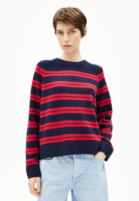 Rot gestreifter Pullover in Navy mit Rundhalsausschnitt und gerippten Bündchen, aus weichem Strickmaterial gefertigt. Getragen mit hellblauen Jeans.