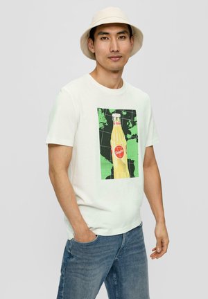 Witte katoenen t-shirt met een afbeelding van een gele frisdrankfles met een rood label op een groen en zwart geruit achtergrond. Strakke spijkerbroek.