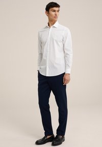 Witte button-up shirt met lange mouwen, gecombineerd met marineblauwe broeken en zwarte loafers. Glad stof, klassieke kraag en slim fit.