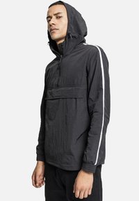Chaqueta con capucha negra y media cremallera, que cuenta con un bolsillo delantero y rayas blancas en los laterales. Tejido texturizado con un diseño ligero.