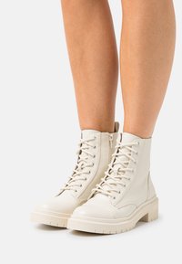 Bottines blanches à talon bas avec une finition en cuir lisse, dotées d'un laçage à l'avant, d'un bout rond et d'une semelle épaisse avec des crampons pour l'adhérence.