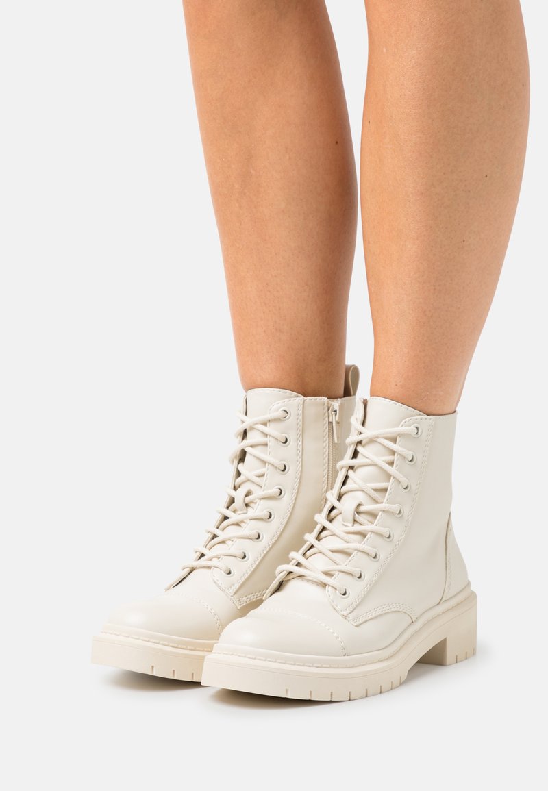 Bottines blanches à talon bas avec une finition en cuir lisse, dotées d'un laçage à l'avant, d'un bout rond et d'une semelle épaisse avec des crampons pour l'adhérence.