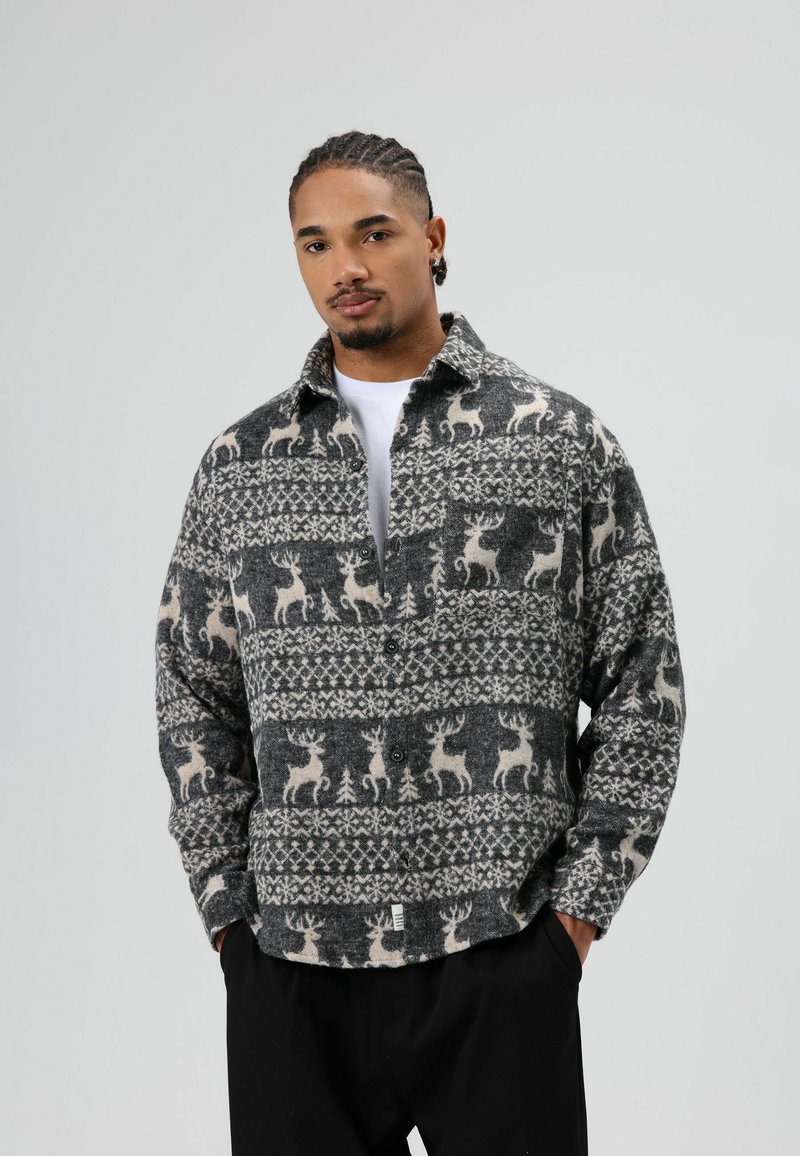 Chemise à carreaux gris et crème avec motifs de rennes et d'arbres. Fabriquée en polaire douce, elle présente un col chemise et un devant boutonné.