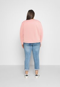 Felpa rosa con texture a coste e collo rotondo, abbinata a jeans azzurri con risvolto e sneaker bianche con dettagli neri.