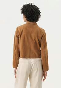 Bruine suède cropped jack met een kraag, lange mouwen en strakke lijnen. De achterkant heeft een gladde textuur en subtiele stiksels.
