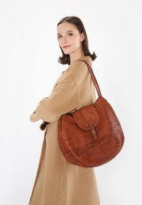 Sac à épaule en cuir marron avec une texture côtelée et un rabat, doté d'une fermeture à boucle métallique et d'une forme courbée, porté à l'épaule.