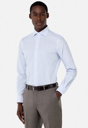 Chemise rayée bleu clair avec un col pointu, fermeture à boutons et manches longues. Associée à un pantalon gris ajusté et une ceinture noire.