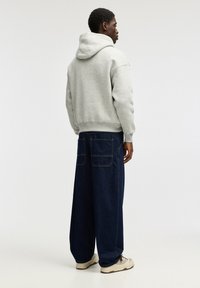 Szary sweatshirt z kapturem w luźnym kroju, w połączeniu z szerokimi ciemnoniebieskimi dżinsami z tylnymi kieszeniami i kontrastowym przeszyciem.