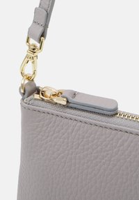 Szara skórzana torebka z teksturowanym wykończeniem, złotymi akcentami i kontrastowym suwakiem. Zawiera odpinany pasek i miękkie wykończenie.