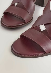 Burgundy leather sandals with crisscross straps, open toe, and a textured heel. Features a smooth surface and stitched detailing.