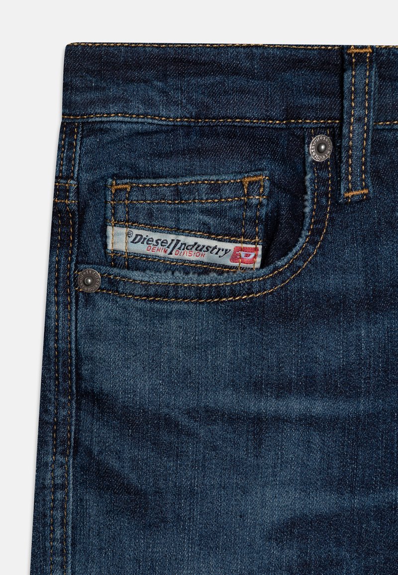 Jeans in denim blu scuro con una piccola tasca frontale, cuciture gialle a contrasto e un'etichetta con "Diesel Industry" sulla vita.