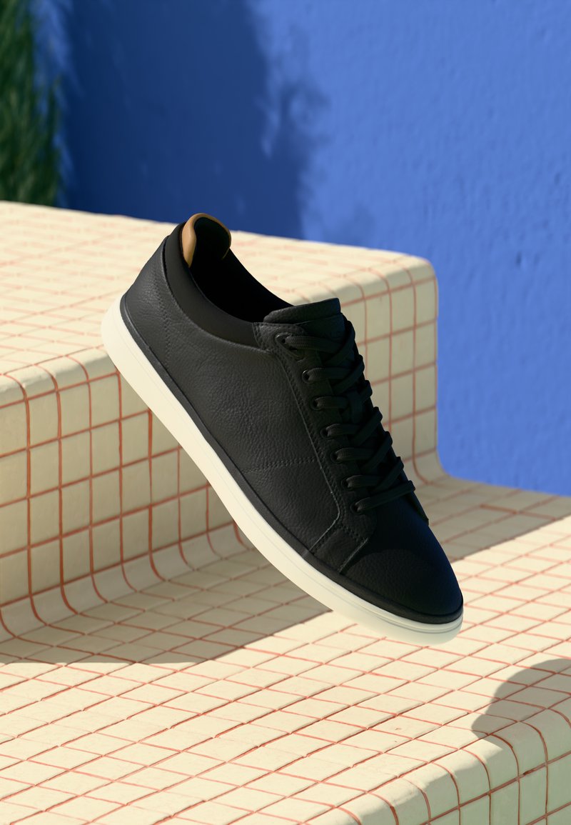 Svart lær sneaker med jevn tekstur, hvit gummisåle og flate lisser. Har en liten hæl og minimalistisk design.